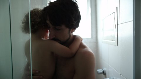 Father entering shower with baby toddler son. Parent and child showering together