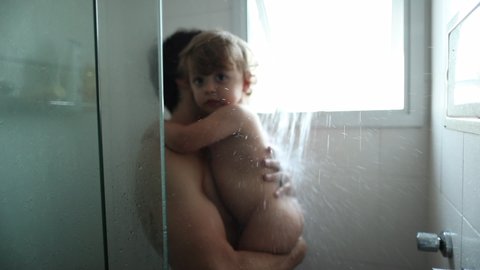 Father holding baby in shower. Parent washing toddler child together