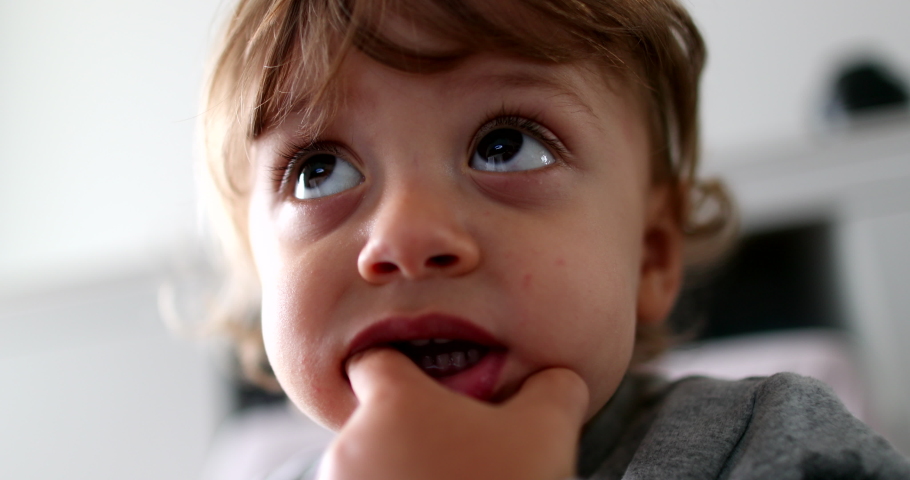 Toddler boy face watching media cartoon. Adorable child baby with hand in mouth hypnotized by screen