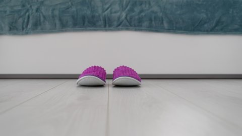 Female feet wearing pink houseshoes at bed on floor, slippers