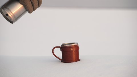 hot tea is poured into a steel mug against a background of white snow. Hiking, fishing, active pastime on a winter day