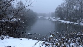 Snow falls on the river with frame of bare branches. Winter landscape. video 4K