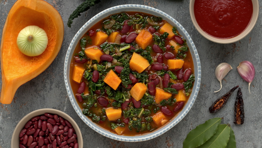 Red bean cooked stew with vegetables: pumpkin, cavolo nero leaves and spices ingredients. Top view, table spin. | Shutterstock HD Video #1084551748