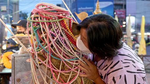 Worshippers whispers their wishes into the ears of a giant brass mouse. Making an offer of beads. Ganesh shrine temple, Huai Khwang, Bangkok, Thailand. Close up 4k, 10bit, 422, 50fps