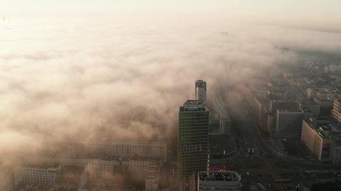 Fly above large city. Busy road between high rise buildings. Morning fog cover illuminated by rising sun. Warsaw, Poland
