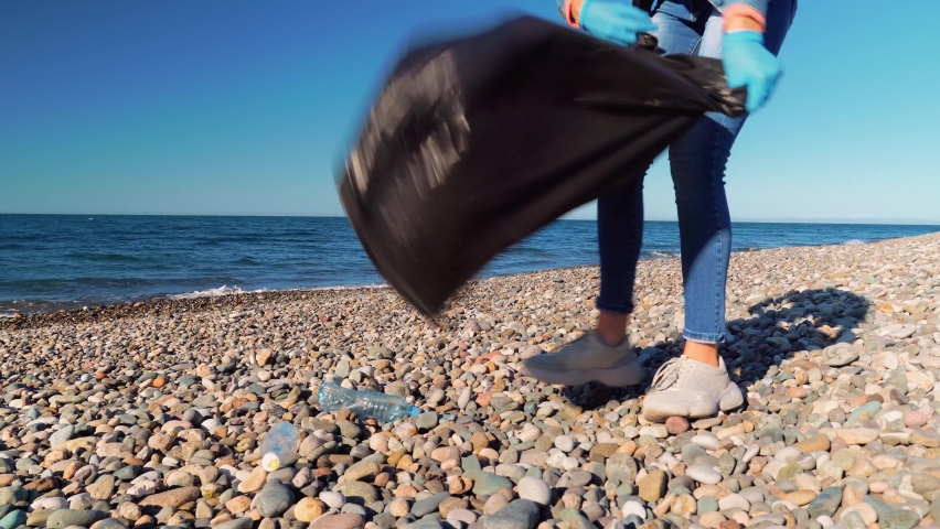 woman collects garbage and plastic on beach. volunteer collects garbage in black garbage bag. Plastic pollution and concept of an environmental problem. Voluntary cleaning of nature from plastic. Royalty-Free Stock Footage #1084556245