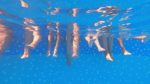 Underwater view of child and parents splashing water with their feet. The holiday joy of a hot summer day. Underwater view of people playing with their feet in blue transparent pool freshwater.Slow.