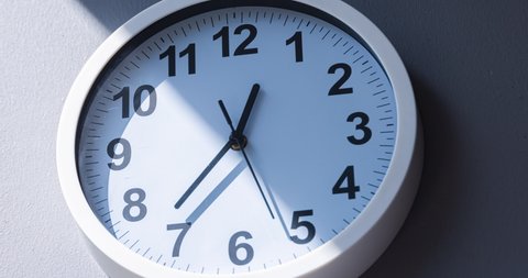 Close up to a wall clock, with running time pointer. Sun and sky reflecting on clock face time passing by. Time lapse on a modern white Clock on white blur background. Wall clock show running time. 