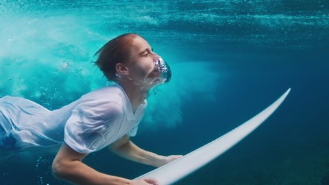 Teen boy dives underwater with surf board and confidently passes the wave