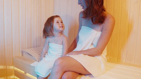 Family sauna. Young woman and toddler girl relax together in the hot wooden sauna