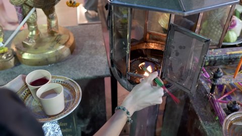 Asian women hand lighting up joss sticks in oil lamp flame. Praying to Ganesh and Trimurti God for love and success. Ganesh Shrine temple, Huai Khwang, Bangkok, Thailand, 4k, 10bit, 422, 50fps