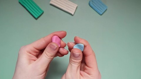 Hands are modeling from blue and pink plasticine. Combining two colors into one.  Green, white, and blue plasticine bricks lie on a green background. 4K