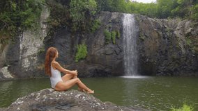 Woman in white bikini looking at the waterfall in jungles. Hiker girl trekking, enjoying beautiful waterfall. Ecotourism concept video, travel girl.