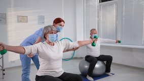 elderly couple exercising on fitballs with muscle specialist in hospital during pandemic, old woman raise arms with support from nurse, masked people - Powered by Shutterstock - Get 15% off with code: PIKWIZARD15