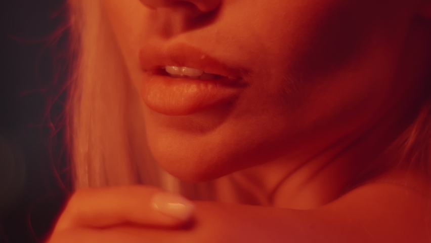 Seductive female lips close up. Mysterious attractive blond woman touching her skin in neon orange light. Soft focus. Royalty-Free Stock Footage #1084573141