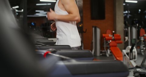 Young handsome athletic man jogging on modern digital display treadmill exercising in the gym alone. Healthy lifestyle, movement and sports