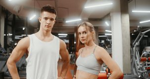 Young man and woman of European appearance in sportswear, looking directly at the camera, standing in the middle of a well-equipped gym, video portraits, close-up