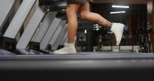 Close-up video footage of a young man of European appearance running on a treadmill in the gym, the frame moving from the man's legs to his face