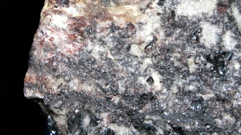 Macro of a quartz-biotite gneiss with quartzitic crystalline layers and zincblende inclusions in a dark rock matrix.