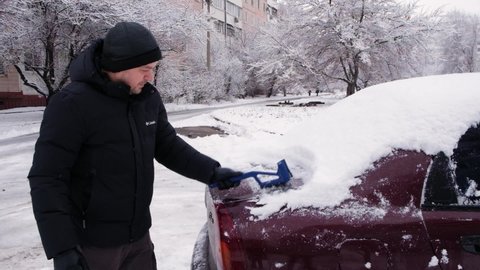 A man clears the car of snow, brushes the snow from the surface in winter. December 28, 2021, Zaporozhye, Ukraine.