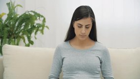 4k video of pregnant woman sitting on the sofa with child clothes.