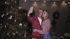 Happy caucasian couple taking selfie photo in front of christmas tree celebrating christmas night together, sending congratulation on mobile phone smartphone, having video call conference 