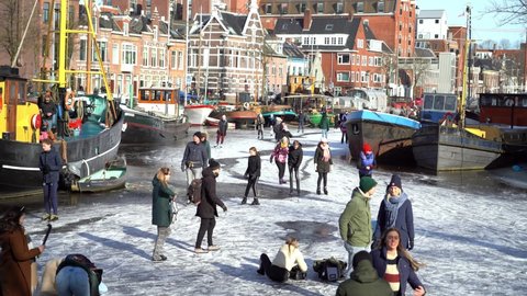 People ice skating on frozen canal in city center in Netherlands. Peoples making pictures, walking and skating on frozen canal in winter. Winter fun in city. Groningen. Netherlands. 14.02.2021