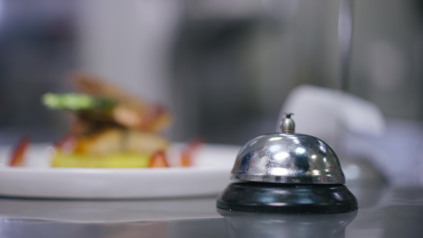 Close-up male finger pushing service bell ringing and hands taking away plate with delicious seafood in restaurant kitchen. Unrecognizable cook and waiter passing order indoors. Service and culinary Royalty-Free Stock Footage #1084601320