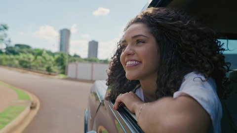 Latin woman in car window. Car trip. Curly hair in wind. Girl looks out of car window. Brazilian travel concept by car. Cinematic 4K