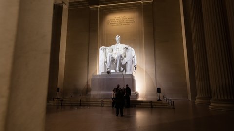 Washington, DC - USA - December 28 2021: Time-lapse of tourists visiting the Lincoln Memorial. The camera tracks rightward from behind a marble column to reveal the statue of Abraham Lincoln.