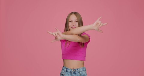 Funny joyful child girl show rock gesture by hands, having fun. Kid rocker make death horns sign on pink background