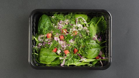 Closing spinach salad close-up. Take away meal top view, Food delivery in closed disposable container, balanced nutrition. Fresh portion in lunch box, vegetarian dish. Healthy eating, diet, catering