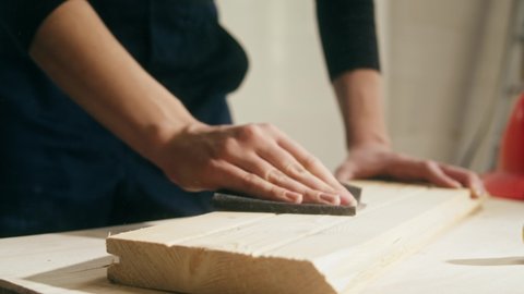 Woman builder sanding wooden board with sandpaper. Female carpenter improving wood surface, making diy furniture. Renovation concept. Building new house or flat.