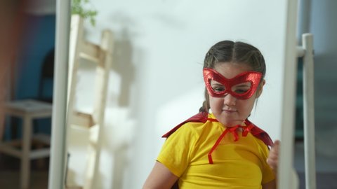 Girl in superhero mask. Child in hero costume. Happy child is winner. Girl is playing at home.Kid in front of mirror in hero mask.Girl play in superhero costume.Successful child with smile on his face