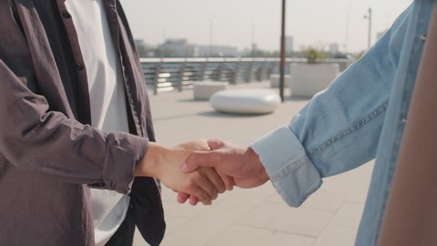 Midsection slowmo shot of unrecognizable business partners shaking hands outdoors in summer