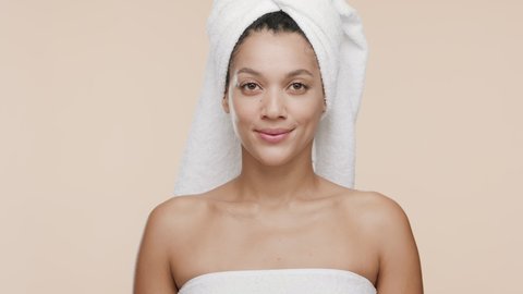 Funny young slim cute African American woman with a towel on her head and bare shoulders throws away orange woman razor smiling wide for the camera on beige background | Unwanted hair removal concept