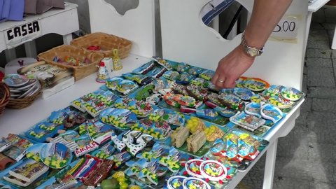Tourist woman is choosing a souvenir, fridge magnet at the outdoor shop or street kiosk in Amalfi town