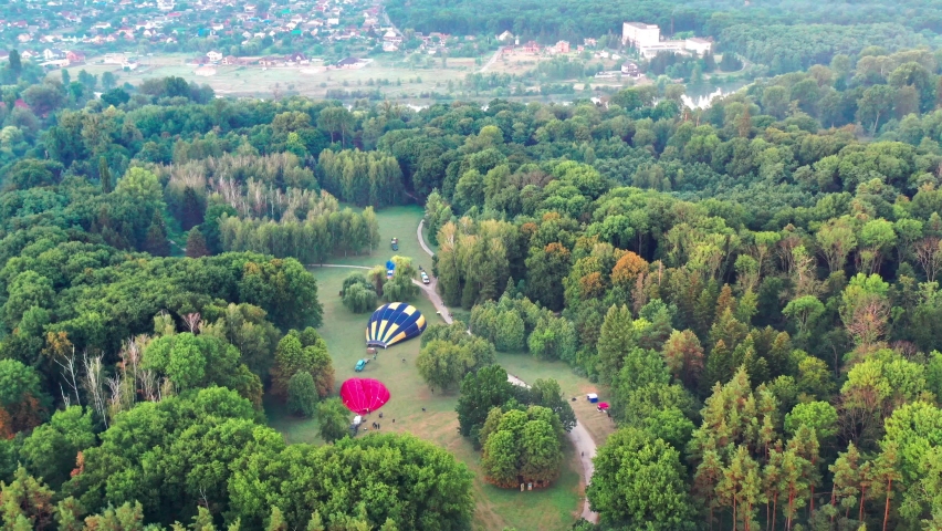 Nice top view of the park, forest covered with greenery. Morning river in fog. Small houses in the background. The balloon is being prepared for flight.