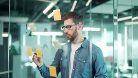 creative young entrepreneur business man in modern office uses post Papers sticky notes to share idea. brainstorming, Bearded thinking male solving strategy Using glass note wall Board. startup posted - Powered by Shutterstock - Get 15% off with code: PIKWIZARD15
