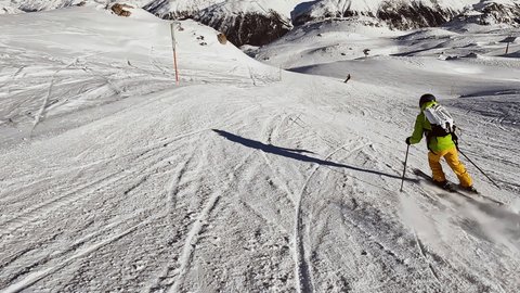 Slow motion: Follow shot, young man skiing downhill on ski slope in the Alps. Action camera filming skier descending technical piste 