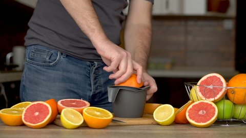 A man is squeezes orange juice with citrus juicer. Close-up of hands, oranges, juicer, healthy lifestyle
