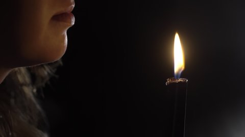 Girl blows out a candle fire in the dark. Woman lips closeup