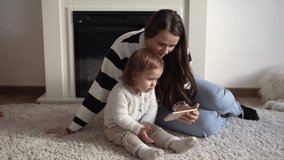 Cheerful adorable toddler kid daughter enjoy learning using smart phone with parental control. Happy family young parent mother mum showing funny cartoon mobile app, watching videos relaxing at home
