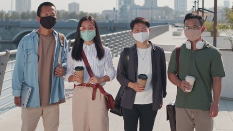 Medium portrait of group of four young Asian friends in casualwear and face masks posing for camera standing at river embankment in summer