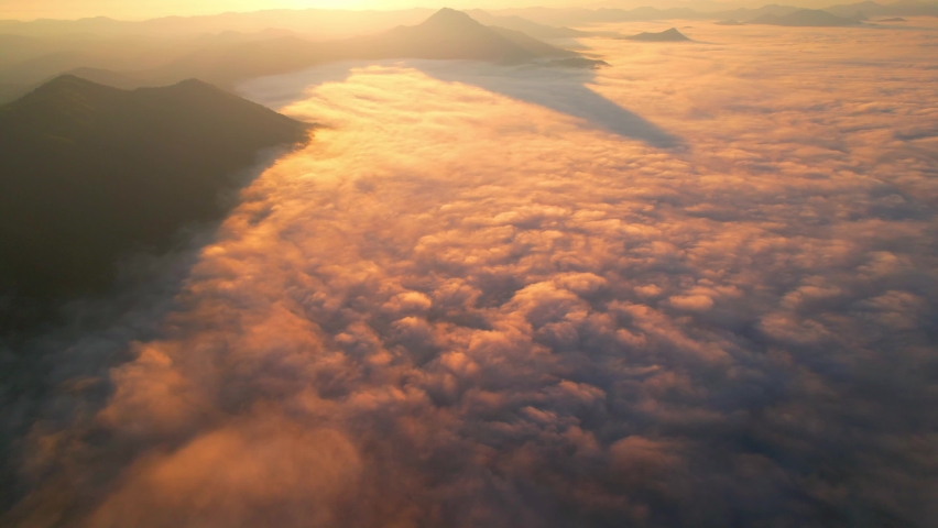 4K Drone flight over the clouds during sunrise. Sun is rising above sea of clouds until the horizon, bright weather and amazing nature landscape
