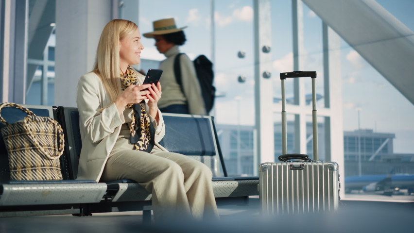 Airport Terminal: Woman Waits for Flight, Uses Smartphone, Browse Internet, Social Media, Online Shopping. Traveling Female Remote Work Online on Mobile Phone in a Boarding Lounge of Airline Hub Royalty-Free Stock Footage #1084637080