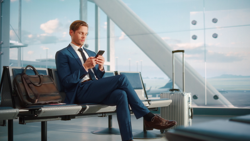 Airport Terminal Flight Wait: Smiling Businessman Uses Smartphone for e-Business, Browsing Internet with an App. Traveling Entrepreneur Work Online on Mobile Phone in Boarding Lounge of Airline Hub Royalty-Free Stock Footage #1084638256