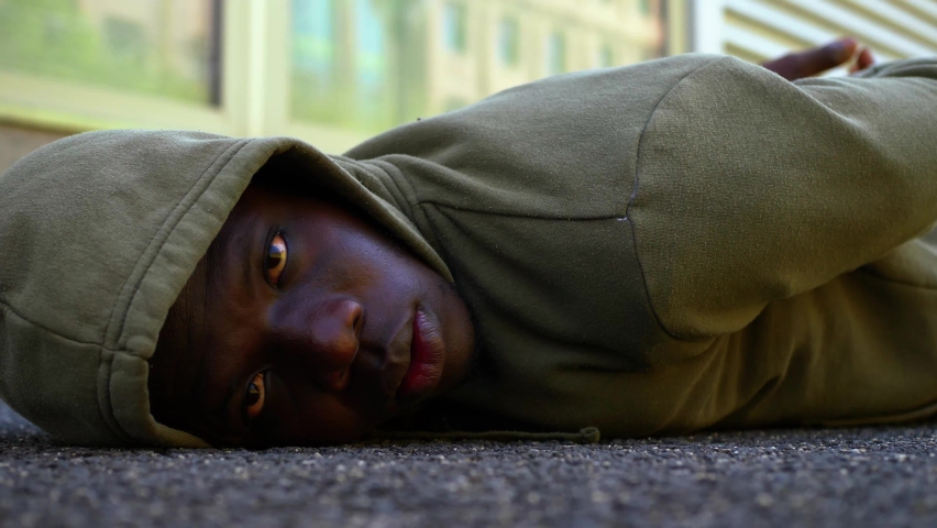 hooded black man lying on the ground stares at camera - protest symbol Royalty-Free Stock Footage #1084644778