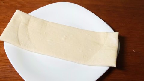 A man makes, rolls rolls of raw dough, wraps on a white plate on a wooden background. Homemade buns.