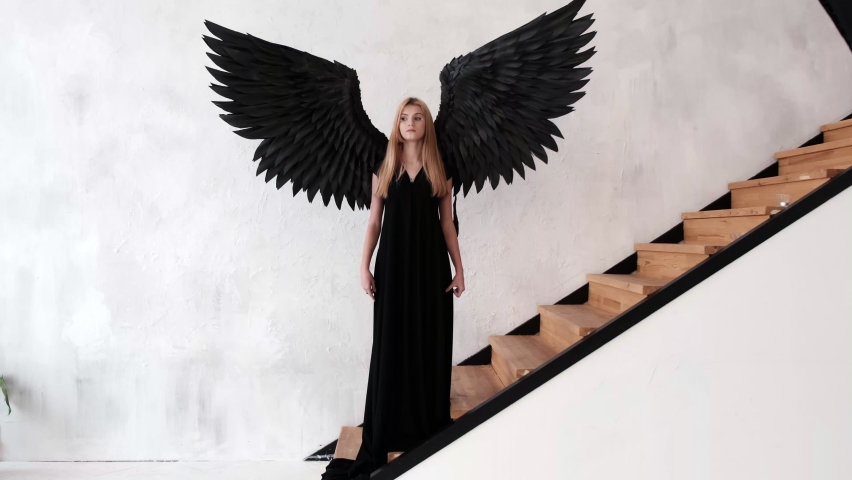 A girl with black angel wings and a black dress stands near the stairs.